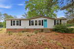 Charming single-story, light gray house with black shutters and a bright turquoise door at 3516 E Thollie Green Road, Stem, surrounded by pine trees and pinecones.