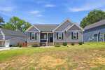 A single-story gray house with white trim and a covered front porch sits on a slightly sloped lawn at 104 Averly Court in Stem, featuring minimal landscaping under a clear blue sky. Neighboring homes are visible on either side.