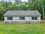 Charming single-story gray house at 126 Hunter Road, Henderson, with black shutters, a white front door, small front steps, and a grassy yard, surrounded by tall trees and dense greenery in the background.