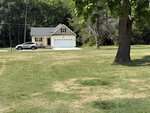 A small beige house at 509 Hicksmill Road in Oxford features a two-car garage at the edge of a large grassy yard, bordered by trees. A silver car is parked in the driveway, and a leafy tree stands in the foreground.