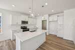 Bright modern kitchen at 109 Millview Way in Franklinton featuring white cabinets, stainless steel appliances, an island with a sink and pendant lights, and wood-look flooring. The space is clean, open, and minimalist in design.