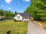Charming single-story beige house at 280 Beaver Ridge Drive, Youngsville, with a dark roof and front porch, set back from the street with a wide driveway and well-kept lawn, surrounded by trees under a blue sky with scattered clouds.