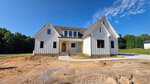 A newly constructed white modern farmhouse at 35 Firefly Lane in Louisburg features a dark roof, large windows, and a front porch, sitting on a dirt lot surrounded by trees under a clear blue sky.