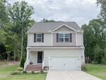 Charming two-story suburban house at 55 Shearin Lane, Youngsville, with beige siding, brown shutters, and a white double garage door. A small porch welcomes you, surrounded by a green lawn and trees.