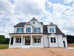 A newly built, two-story white house with grey roof, multiple gables, and large windows sits on a bare dirt lot at 160 Broadleaf Lane, Youngsville, featuring a covered front porch under a partly cloudy sky.
