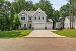 Beautiful two-story gray house with white trim and stone accents at 101 Yuma Drive, Louisburg. Features a three-car garage, large concrete driveway, green lawn, trees in the background, and a small shed to the right side.