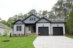 Single-story gray house at 117 Deer Cross Drive, Louisburg, with black garage doors, stone accents, and white trim. Surrounded by a green lawn and tall trees, it features a wooden frame on the front porch and a wide driveway.