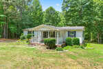 A single-story white house at 2145 Antler Way Lane in Creedmoor features a small front porch with steps, surrounded by green bushes and trees on a grassy lawn under a blue sky.