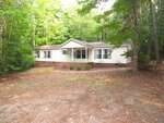 Charming single-story beige house with white trim and large front windows at 351 Winding Acres Way in Franklinton. Set on a brick foundation, it features a small covered porch and is surrounded by tall green trees and a dirt yard.