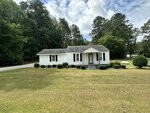 A small white house with dark shutters and a covered porch sits on a spacious, grassy lawn at 560 Clyde Pearce Road in Zebulon, surrounded by trees under a partly cloudy sky.