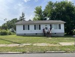 A small, single-story white house with black shutters and a front porch sits at 601 N Chestnut Street in Henderson. The grassy lawn is bordered by a sidewalk, with tall green trees behind the house under a partly cloudy sky.