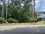 A view of a paved street in Louisburg with dense green trees and shrubs on the left and a modern two-story house at 190 Buckaroo Drive, featuring dark siding and white trim, partially visible under a cloudy sky.
