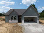 A newly constructed single-story house at 6216 Carole Drive in Oxford features gray siding, a covered front porch, and an attached two-car garage. The driveway and lawn remain unfinished, with exposed dirt and construction materials in the garage.