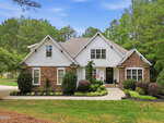 A two-story suburban house with white siding and brick accents at 60 Granite Drive in Franklinton, surrounded by neatly trimmed bushes and trees. An American flag hangs near the front door, and a curved driveway leads to the entrance.