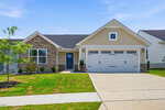 Charming single-story suburban house at 100 Shorebird Lane in Franklinton, featuring beige siding, stone accents, an attached two-car garage with white doors, a neatly trimmed lawn, a small front porch, and a young tree under a clear blue sky.