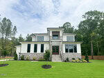 Modern two-story house at 20 Cherry Bark Drive in Youngsville, featuring large windows, stone and white siding exterior, double front doors, landscaped lawn, and surrounded by tall trees under a partly cloudy sky.