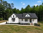 A modern farmhouse at 3205 Old US Highway 64, Spring Hope, with white siding, black trim, and a dark roof. Enjoy the front porch, landscaped yard, and scenic views of tall trees and blue sky from this charming rural retreat.