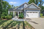 A modern, single-story house at 3809 Watermark Drive, Franklinton, features gray siding, a covered front porch, white trim, and a double garage. A concrete driveway curves to the porch amid green shrubs and tall trees in the background.
