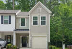 A two-story beige townhouse at 1416 Chatuga Way, Wake Forest, with white trim, black roof accents, and a one-car garage. Two upstairs windows and a black front door with side windows overlook green trees and a well-kept lawn.
