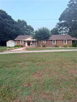 A single-story brick house at 823 Abbott Road in Henderson with a front porch, bushes, and a tree in the yard. A small white shed sits to the left, surrounded by green grass and large trees in the background.