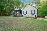 Charming single-story beige house at 4115 Geneva Drive, Franklinton, with black shutters, a covered front porch, and flower boxes. Surrounded by trees and a large grassy yard with a driveway along the right side.