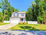 A two-story gray house at 30 Nandina Lane in Youngsville with a white garage and fenced yard, set on a sunny day with green trees behind and a well-kept lawn in front. An American flag hangs near the entrance.