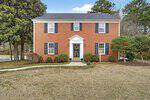 A two-story red brick house at 2064 Oxford Road, Henderson, features black shutters, white trim, and a centered front door framed by white columns. The yard has trimmed bushes and patchy grass, with a sidewalk curving toward the entrance.