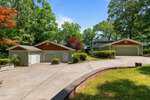 A wide concrete driveway at 373 Sagamore Drive in Louisburg leads to two separate green garages with white doors, surrounded by trees and shrubs, with a two-story house visible in the background under a clear, blue sky.