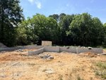 A concrete foundation is under construction on a dirt lot at 3738 US 401 Highway N in Louisburg, surrounded by trees and greenery, with a storage container and construction materials visible in the background.