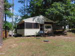 A small beige house at 110 Cimarron Drive, Louisburg, features a screened porch nestled among tall trees and grass on a slightly sloped lot. The partially shaded yard includes two round septic lids visible in front of the house.