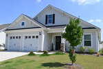 A modern two-story house with white siding, black roof, double garage doors, and a small covered porch welcomes you at 113 Sugarmaple Way in Youngsville, complete with steps and a young tree adorning the sunny front yard.