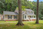 Charming two-story beige house at 119 E Stratford Drive, Henderson, with black shutters, a front porch with white railings, and a side extension. Surrounded by trees and a grassy yard, plus a paved walkway leading to the entrance.