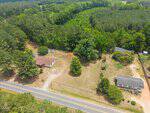 Aerial view of a rural property on 0 Person Road in Louisburg, featuring two houses, a large grassy yard, several trees, and a paved road in front, all surrounded by dense forest.