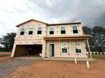 A two-story house under construction at 60 Mistflower Drive in Youngsville features exposed sheathing, window openings, and an unfinished garage. The ground is bare dirt, with trees visible in the background beneath a cloudy sky.