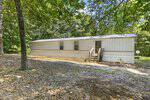 A beige mobile home with a metal roof sits among trees at 441 Hunter Road, Henderson. There are three windows, a door with steps leading up, and a yard covered in dirt and fallen leaves; a satellite dish is visible in the background.