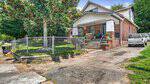 Located at 124 Granite Street in Henderson, this brick house features a covered front porch, steps to the entrance, and a chain-link fence enclosing a yard with a large tree. A white truck is parked in the driveway beside the house.