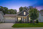 A modern, single-story house in Youngsville with a two-car garage, stone accents, a covered front porch, and a well-maintained lawn at 112 Sweetbay Park, set against trees at dusk with a purple and blue sky.