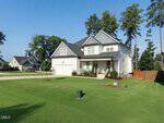 Charming two-story white house with gray roof at 15 Kathleen Court, Youngsville, featuring a front porch, attached garage, and a large manicured lawn bordered by tall trees in a sunny suburban neighborhood.