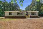 Charming single-story beige house with dark shutters at 2554 Conyers Road, Franklinton. Features a front porch and steps, set in a spacious yard with pine needles and tall trees under a clear blue sky.