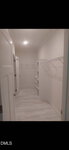 This long, narrow walk-in closet at 235 Joe Ayscue Road, Henderson features white walls, tiled floor, open shelving, and wire racks for hanging clothes. The space is well-lit with a ceiling light and has a closed door at the far end.