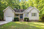 A single-story beige house with white trim at 114 Cherokee Drive, Louisburg, featuring a front porch, blue front door, attached garage, and brick foundation, surrounded by green grass and tall trees.