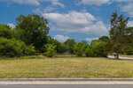 A grassy empty lot bordered by trees and bushes under a partly cloudy sky, with a road and sidewalk in the foreground, located at 613 Broad Street in Oxford.