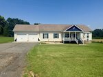Single-story beige house located on 9200 Grassy Creek Road in Bullock, featuring a welcoming front porch, two-car garage, and a neatly trimmed lawn under a clear blue sky with trees in the background.