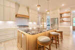 Modern kitchen with cream cabinets, wood accents, marble island with sink, three round stools, stainless steel appliances, open shelves, pendant lights, and light wood flooring.