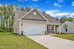 A modern single-story house with a gable roof, double garage, beige siding, and stone accents sits on a neat lawn under a blue sky with scattered clouds at 1109 Rhino Bend in Oxford.