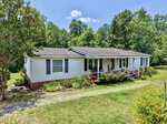 A white, single-story house with a covered front porch, surrounded by green trees and bushes, sits on a grassy lawn under a blue sky at 1702 Mineral Springs Drive in Stem.