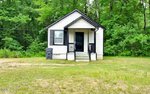 Charming small white house with black trim and a front porch, nestled at 110 Cleveland Street in Henderson, surrounded by grass and dense green trees in the background.