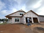 A newly constructed house on 92 Moon Flower Walk in Youngsville features an unfinished exterior, exposed framing, and a garage. The yard is bare dirt, with a "For Sale" sign positioned near the driveway. Above, the sky is partly cloudy.