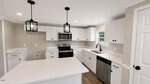Modern kitchen at 102 Pineview Drive, Louisburg, featuring white cabinets, stainless steel appliances, black fixtures, a center island, wood floor, two pendant lights, and a window above the sink letting in natural light.