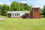 Single-story house at 2278 White Level Road in Louisburg with red brick and white siding, green metal roof, two chimneys, carport on the left, surrounded by green grass and trees under a partly cloudy sky.